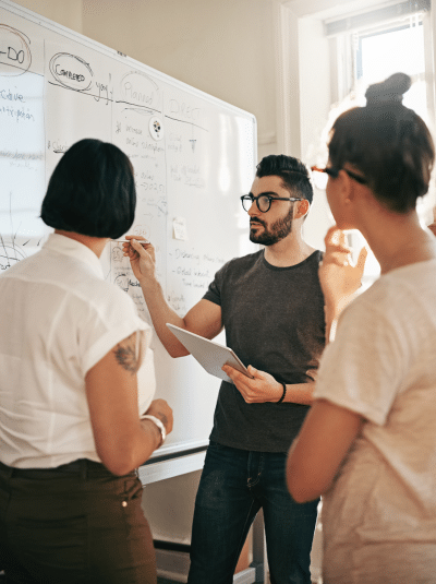 Équipe de travail en réunion devant un tableau blanc rempli de notes - Formations et ateliers | Marie-Andrée Roy, Services conseil et Design Thinking